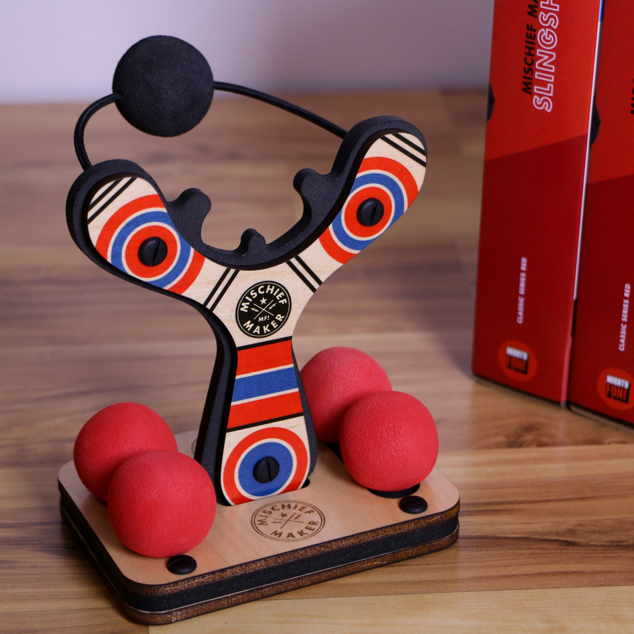 Red Classic wood slingshot with 4 soft foam balls in display stand. Mischief Maker by Mighty Fun!