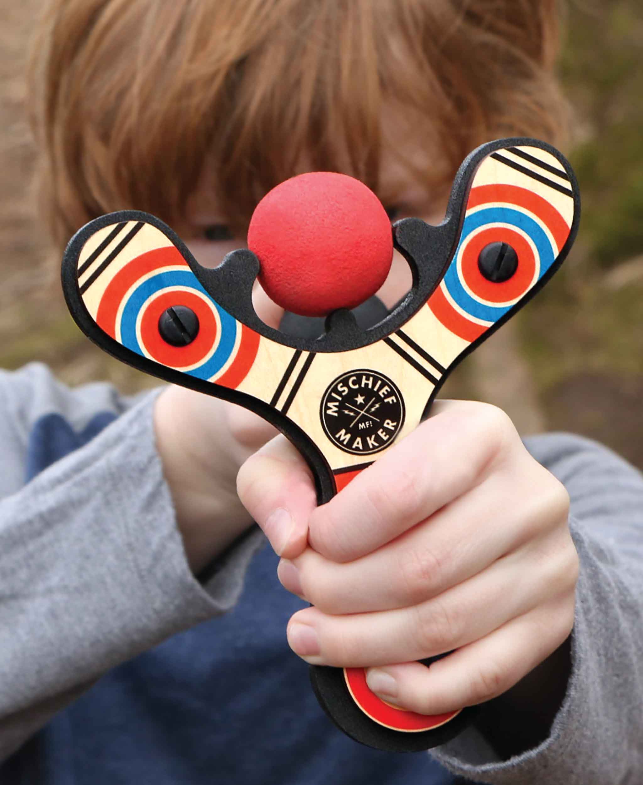 Red Classic wood slingshot being shot by 8 year old boy. Mischief Maker by Mighty Fun!