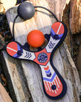 Orange Classic wood slingshot outside on a log. Mischief Maker by Mighty Fun!