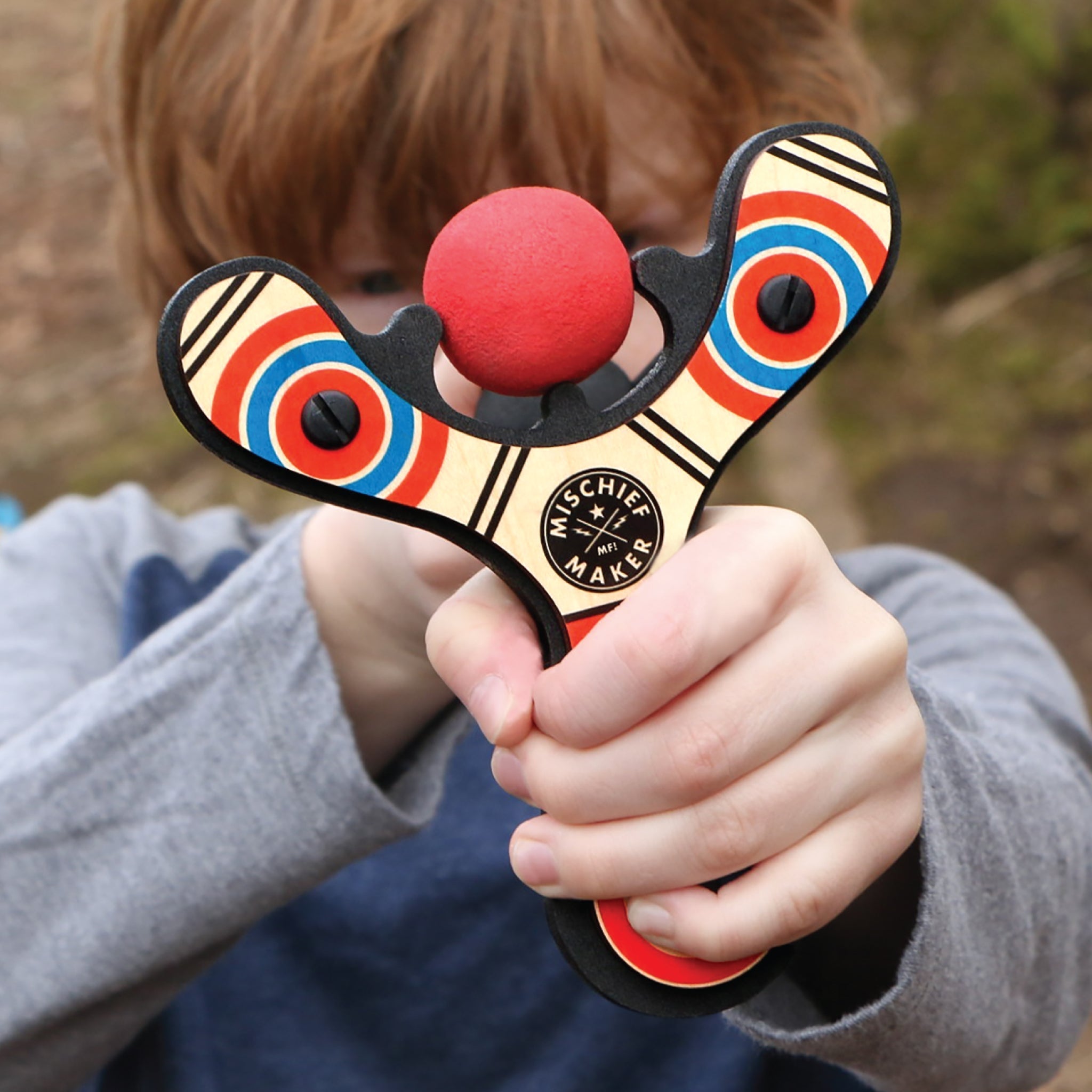 Red Classic wood slingshot being shot by 8 year old boy. Mischief Maker by Mighty Fun!