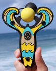 Yellow Surf’s Up toy slingshot hand held by the ocean. Mischief Maker by Mighty Fun!