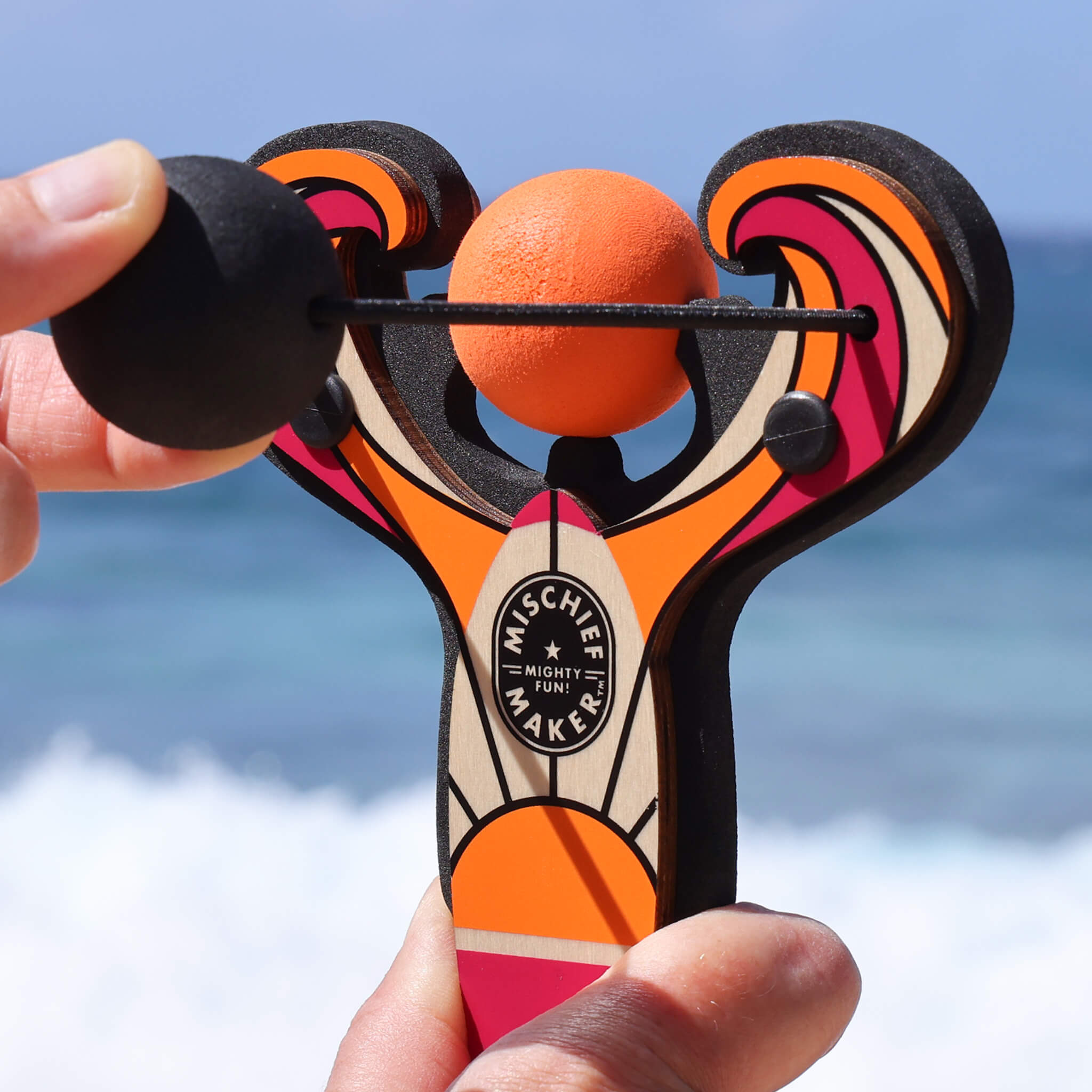 Orange Surf’s Up toy slingshot being launched by the ocean. Mischief Maker by Mighty Fun!