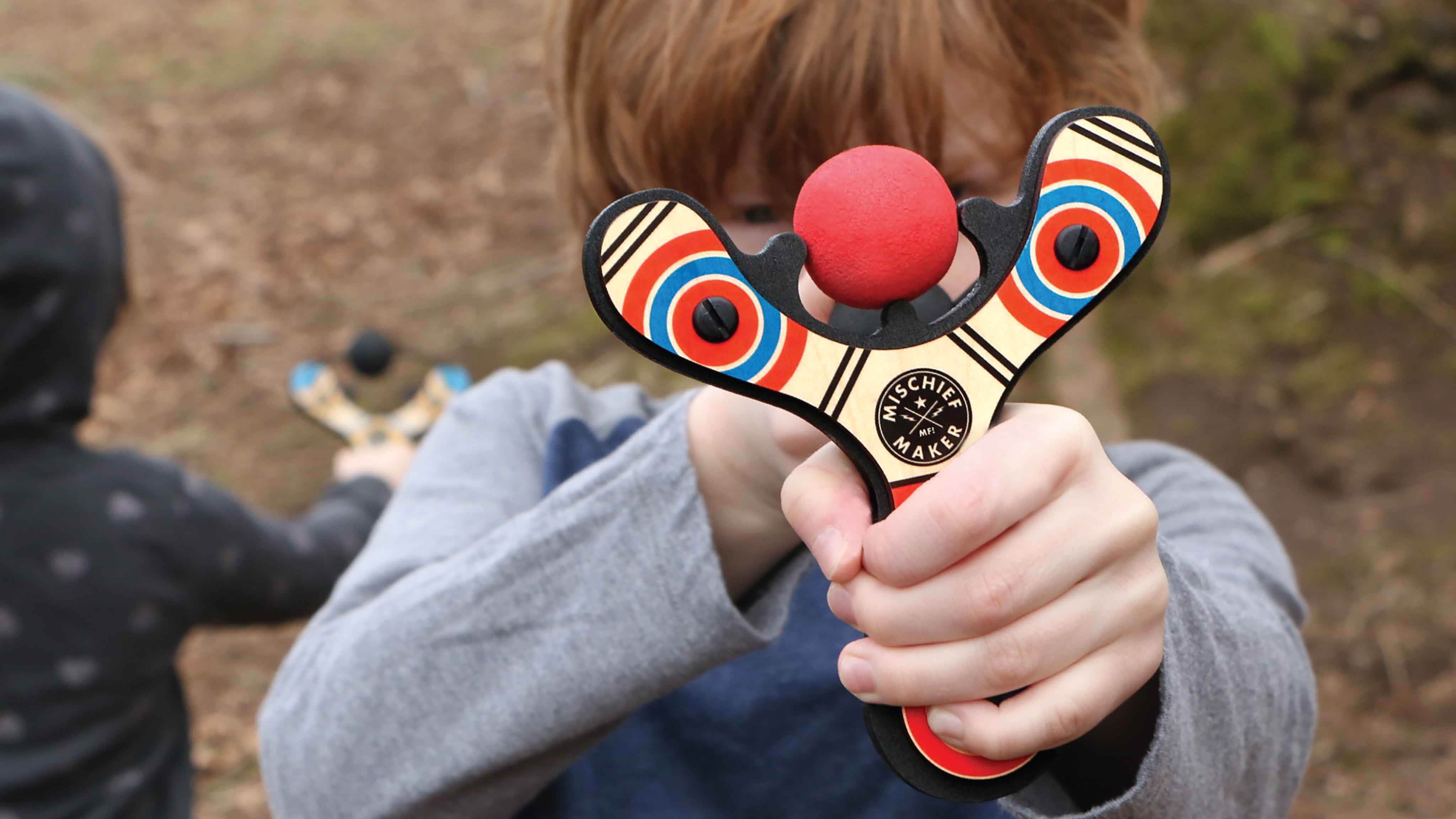 Red Classic wood slingshot being shot by 8 year old boy. Mischief Maker by Mighty Fun!