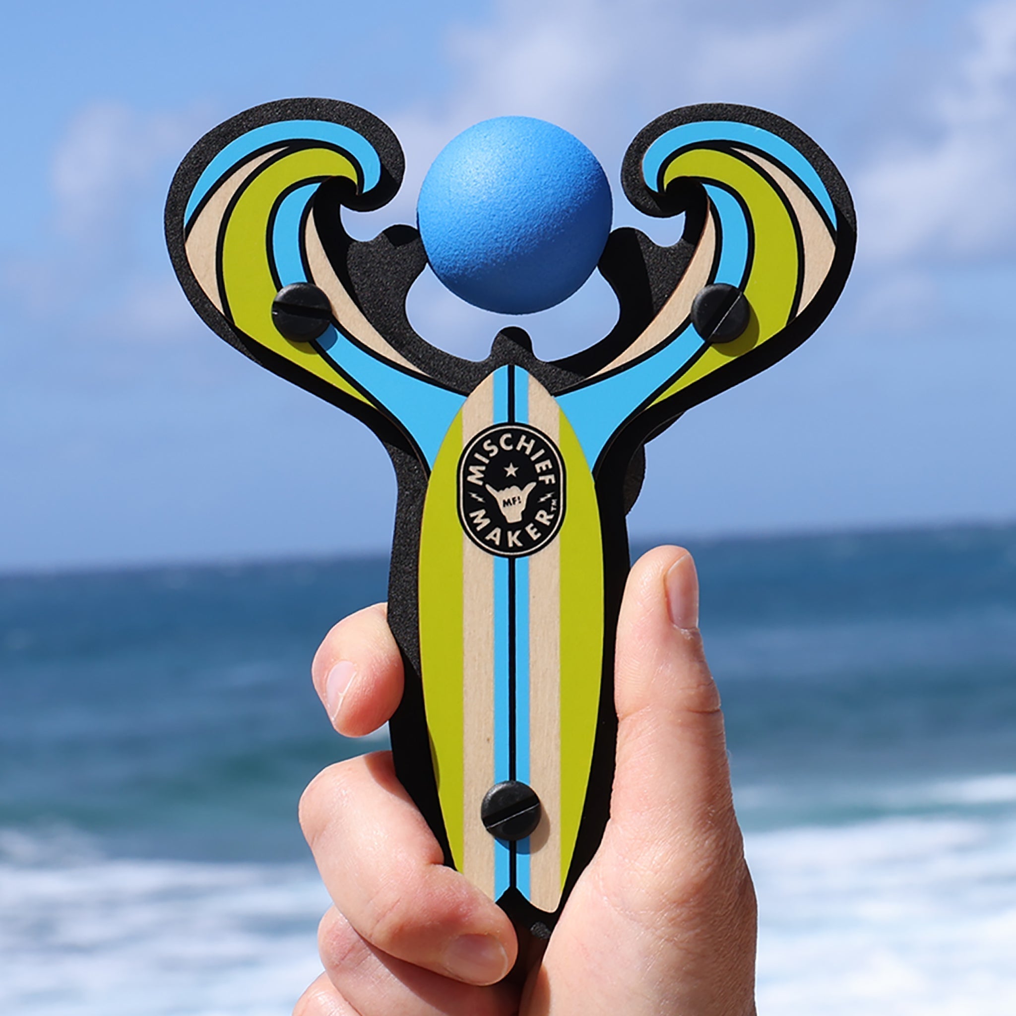 Blue Surf’s Up toy slingshot hand held by the ocean. Mischief Maker by Mighty Fun!