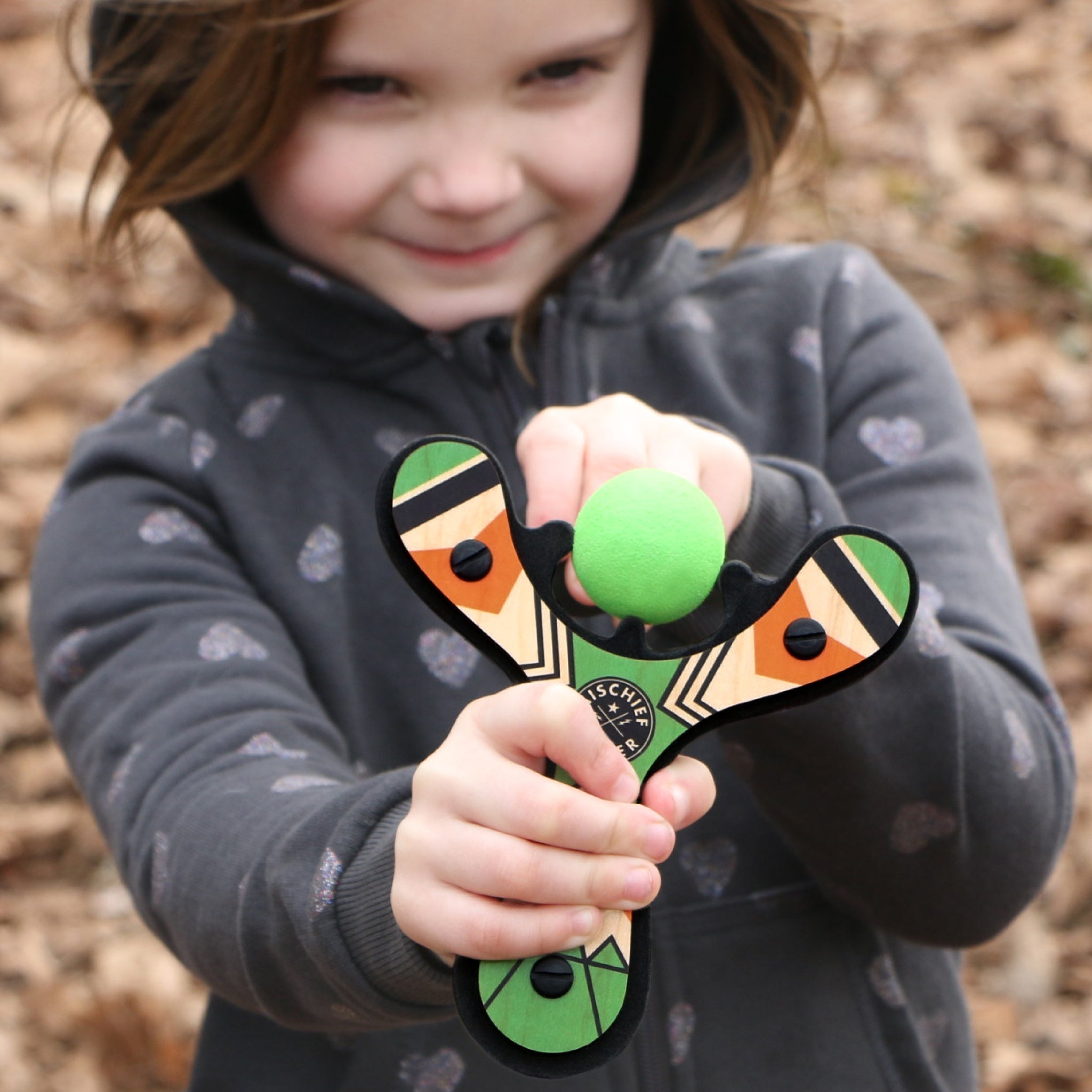 Green Classic wood slingshot being shot by 5 year old girl. Mischief Maker by Mighty Fun!