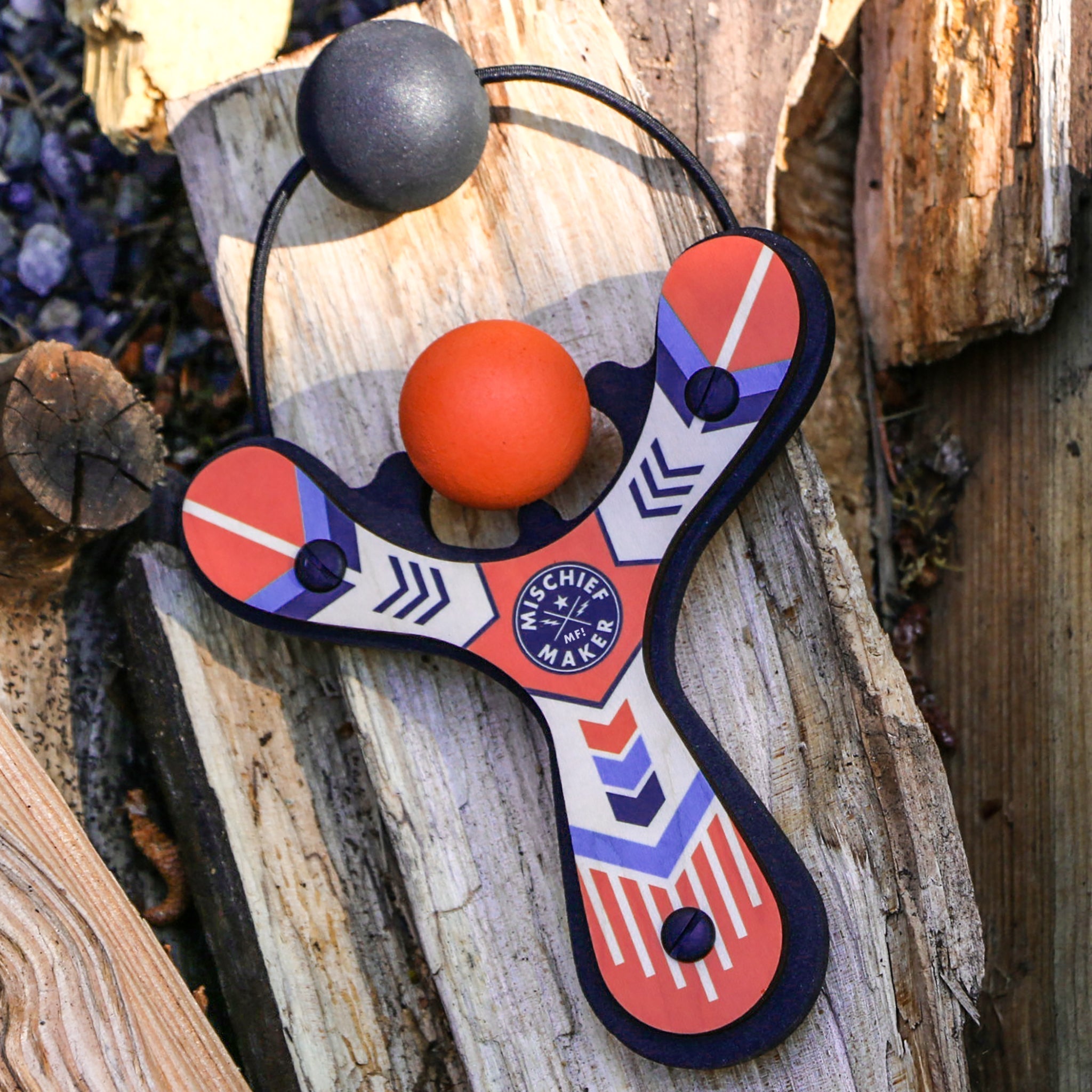 Orange Classic wood slingshot outside on a log. Mischief Maker by Mighty Fun!