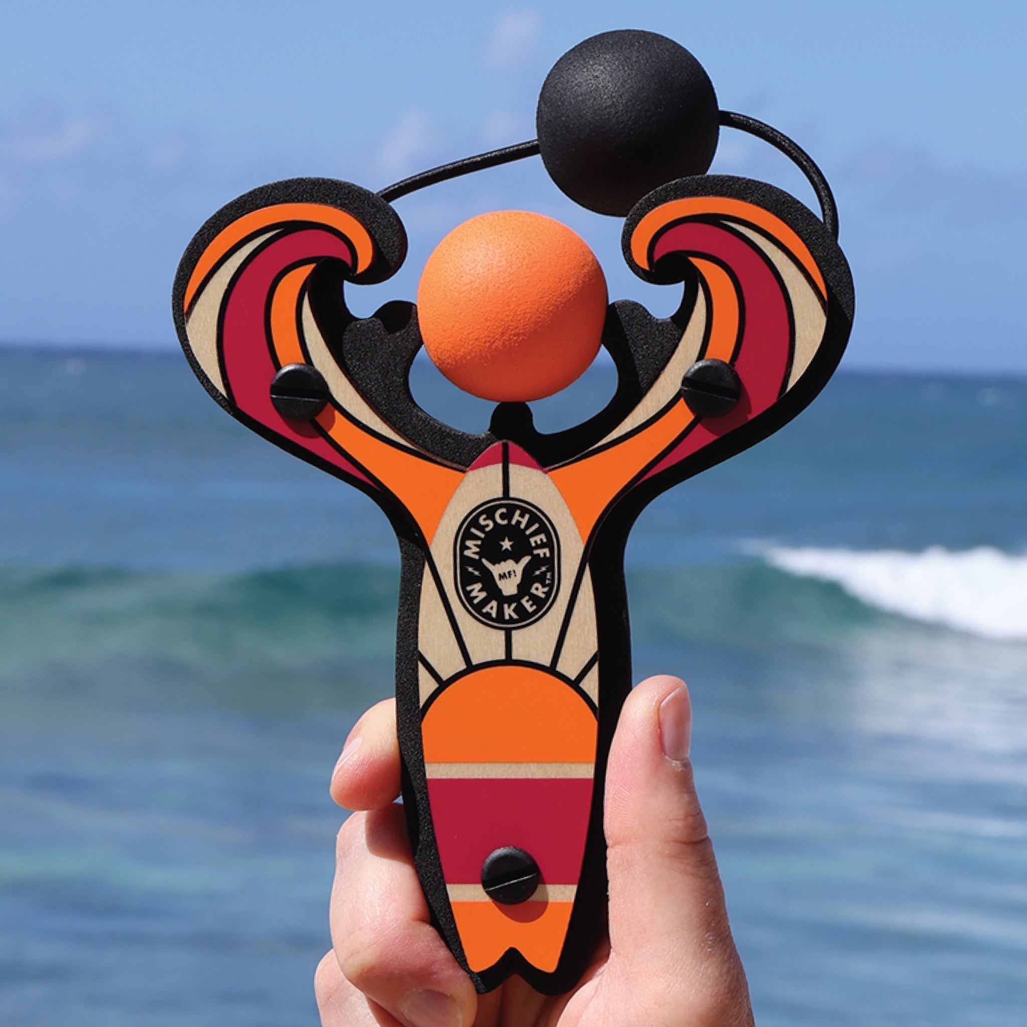 Orange Surf’s Up toy slingshot hand held with ball foam ball by the ocean. Mischief Maker by Mighty Fun!