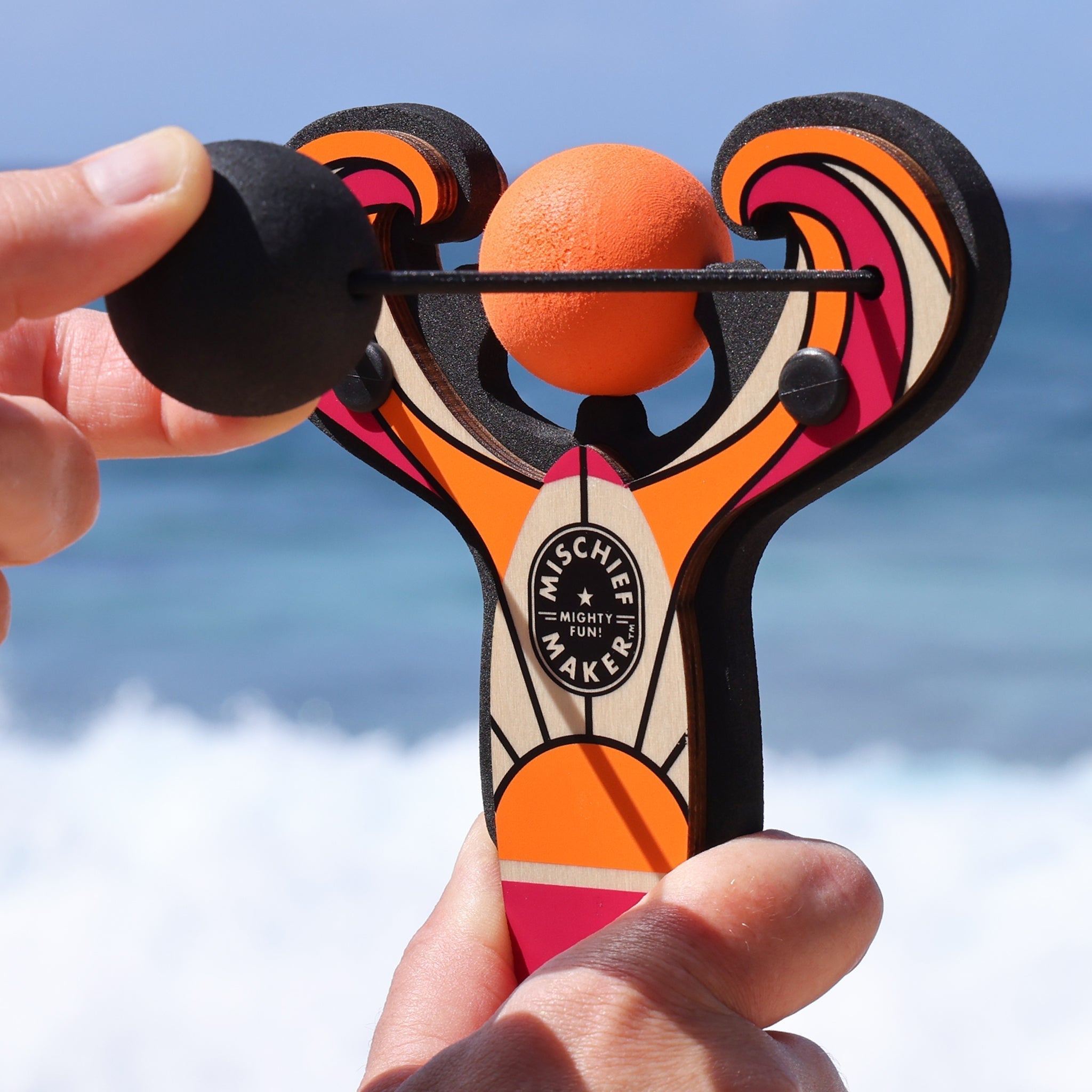 Orange Surf’s Up toy slingshot being launched by the ocean. Mischief Maker by Mighty Fun!