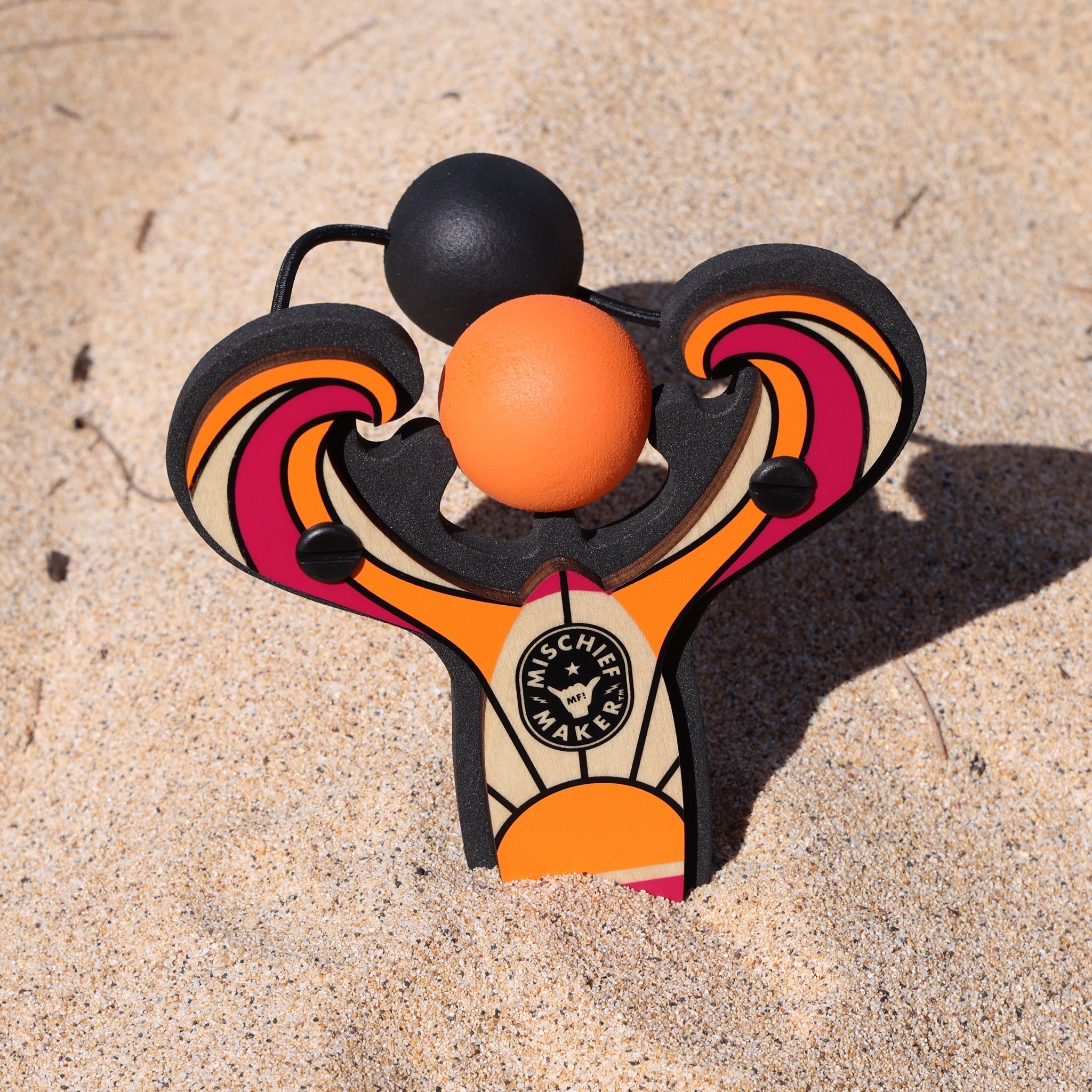 Orange Surf’s Up toy slingshot in the sand on the beach. Mischief Maker by Mighty Fun!